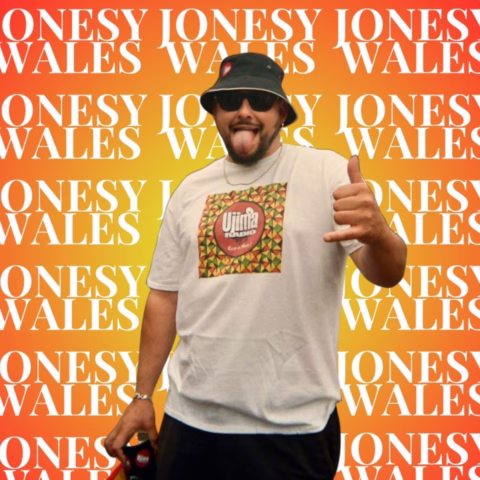 A man in sunglasses and a bucket hat poses with his tongue out and a shaka sign in front of a vibrant orange background repeatedly displaying the words JONESY WALES. He wears a white T-shirt with a colourful logo.