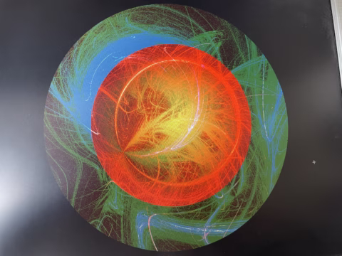 Bright, multicoloured abstract digital art with swirling red, yellow, green, and blue lines forming layered circular patterns against a black background. The vibrant colours create a sense of movement and depth.