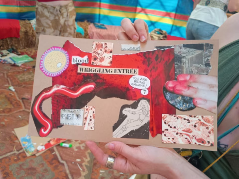 A person holds a collage featuring images of blood, flesh, a wriggling worm, anatomical drawings, and handwritten words like blood and WRIGGLING ENTRÉE, along with various textures and cut-out illustrations.