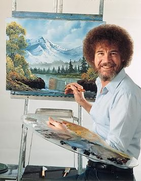 A man with curly hair and a beard smiles whilst painting a landscape with mountains, trees, and a lake on a canvas. He holds a palette and brush, standing at an easel.