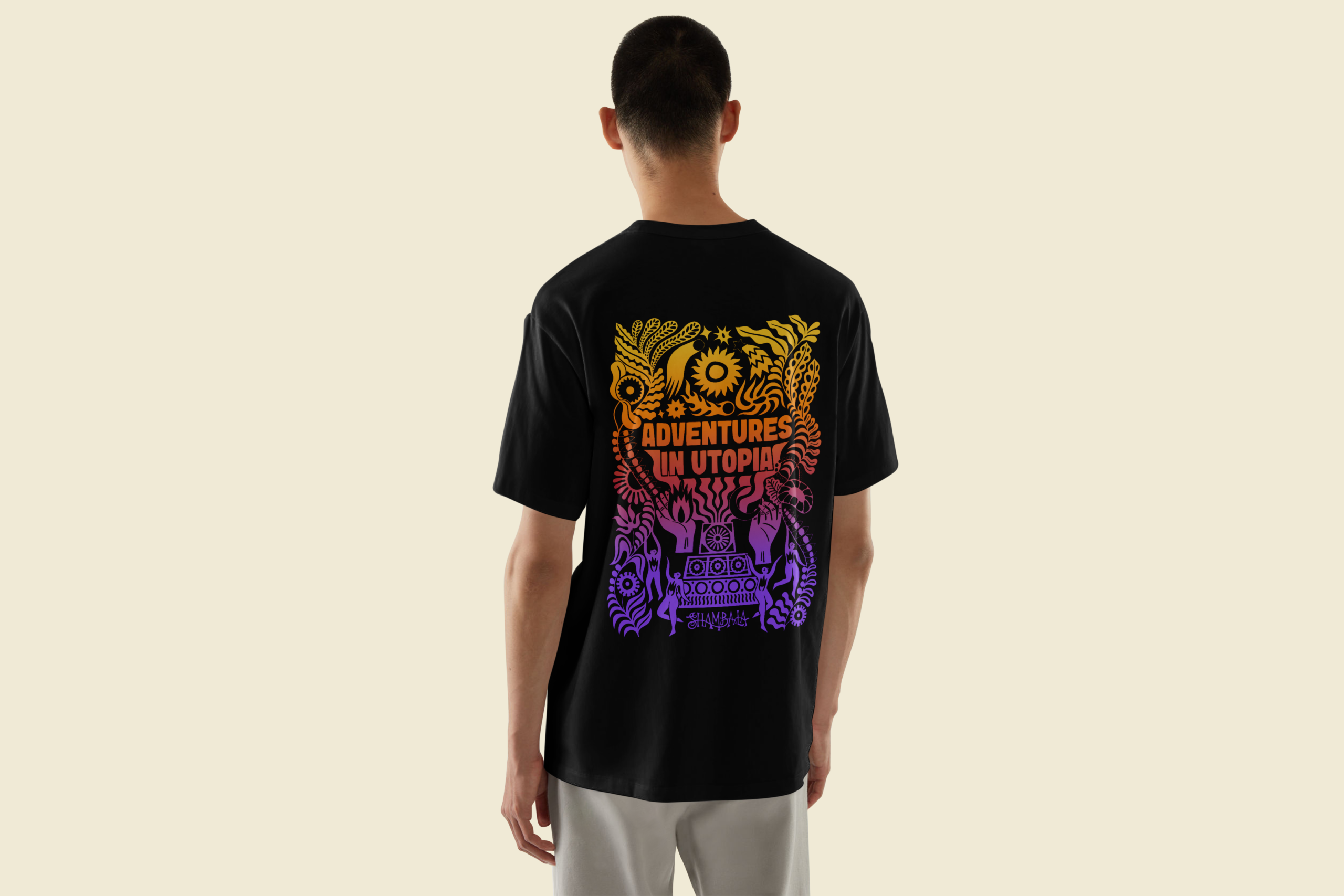 A person faces away, wearing the TSHIRT: SHAMBALA x SOPHIE BASS featuring colourful, stylised graphics of plants, animals, and geometric shapes in orange, pink, and purple with 'Adventures in Utopia' on the back.