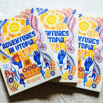 Three vibrant SHAMBALA 2026 PRINTED PROGRAMME booklets, featuring abstract floral and hand-drawn designs in blue, yellow, and orange, displayed on a light fabric background.
