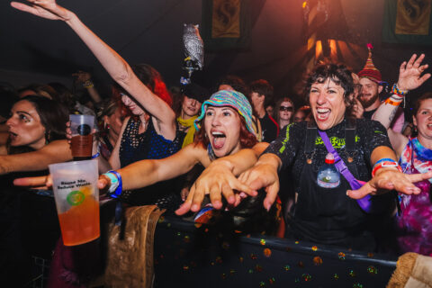 A crowd of people at a music event with their arms outstretched, some holding reusable plastic cups.